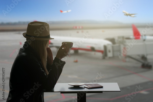 Cup of coffee at the airport.Young woman is drinking coffee in airport.Airline passenger in an airport lounge drinking coffee and waiting for flight aircraft. Caucasian woman with glass if hot coffee.