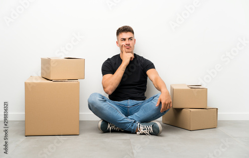 Handsome young man moving in new home among boxes thinking an idea