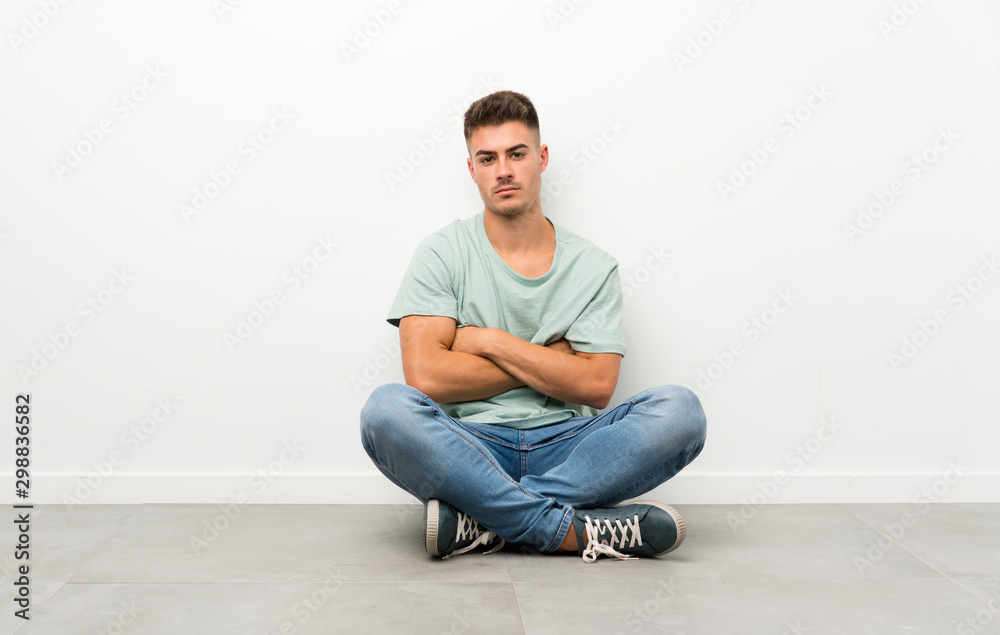 Young handsome man sitting on the floor keeping arms crossed