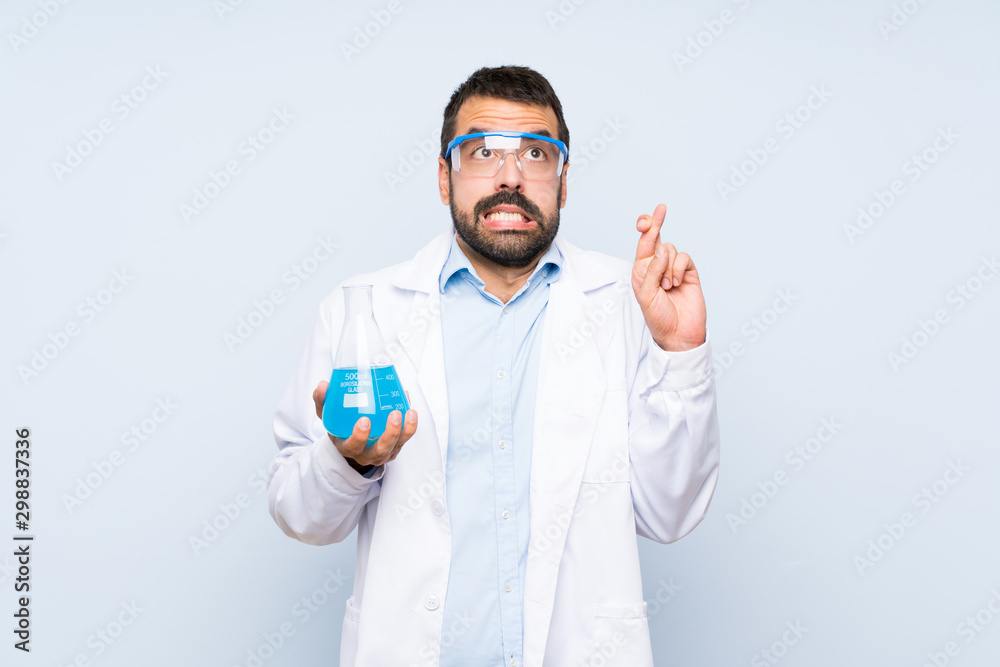 Young scientific holding laboratory flask over isolated background with fingers crossing and wishing the best Young scientific holding laboratory flask over isolated background with fingers crossing and wishing the best