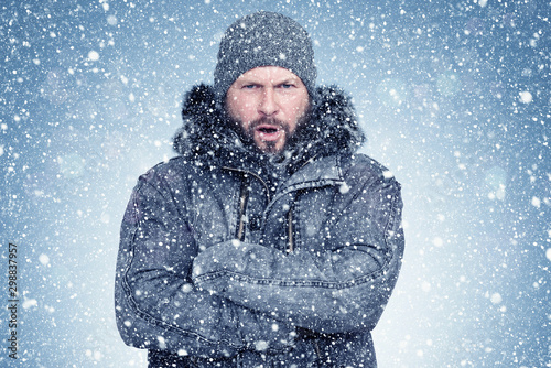 Frozen bearded man in a sheepskin coat and hat warms his hands, cold, snow, frost, blizzard 