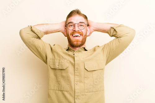 young red head man looking happy, carefree, friendly and relaxed enjoying life and success, with a positive attitude against beige background photo