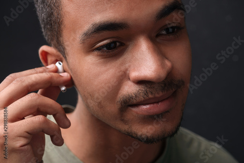 Image of young african american guy using earpods and looking forward