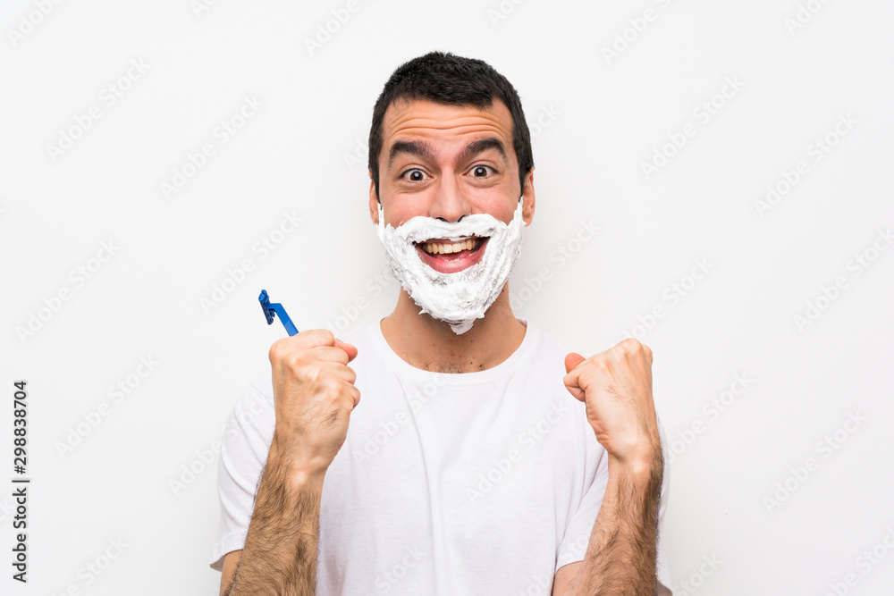 Man shaving his beard over isolated white background celebrating a victory in winner position