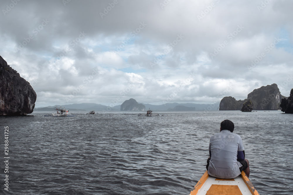 Fototapeta premium Tourist guide sitting on the nose of a fisherman boat observing boats in rocky sea in El Nido Palawan Island the Philippines