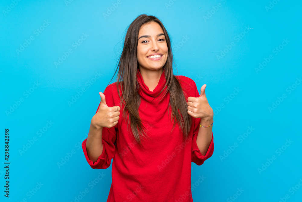 Young woman with red sweater over isolated blue background giving a thumbs up gesture - obrazy, fototapety, plakaty 