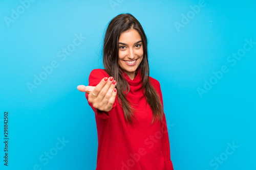 Young woman with red sweater over isolated blue background inviting to come photo