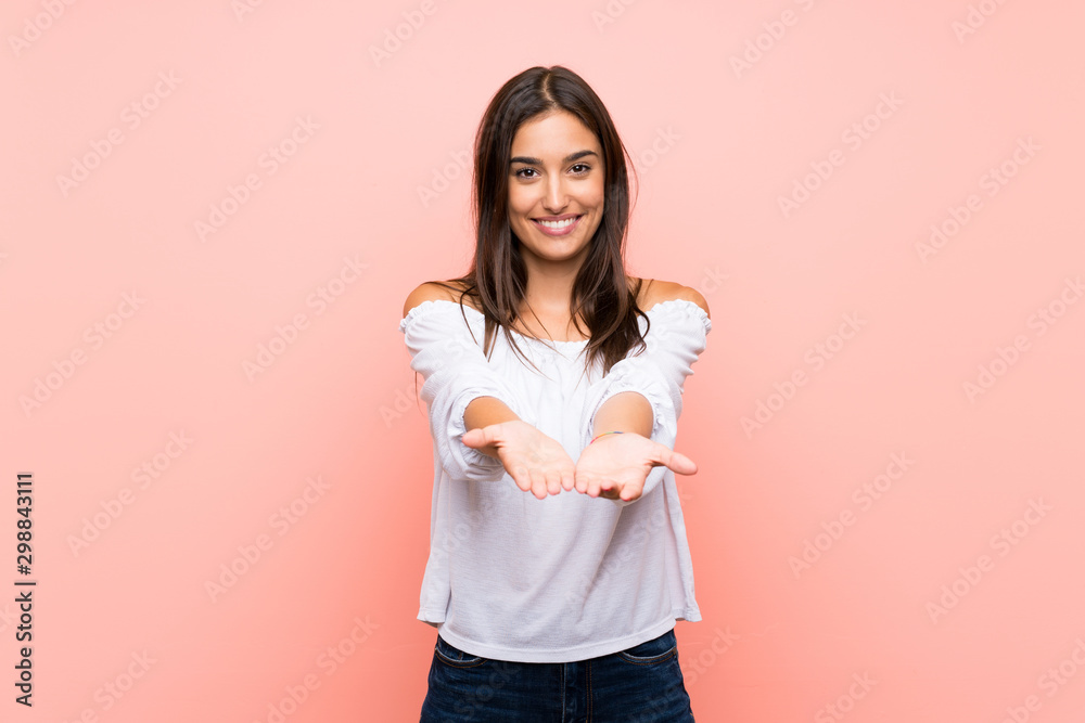 Young woman over isolated pink background holding copyspace imaginary on the palm to insert an ad - obrazy, fototapety, plakaty 