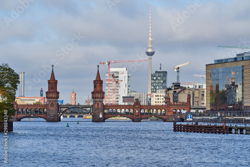 Die Berliner Oberbaumbrücke überspannt die Spree im Morgenlicht mit dem Rathaus, dem Fernsehturm und mehreren Baukränen im Hintergrund