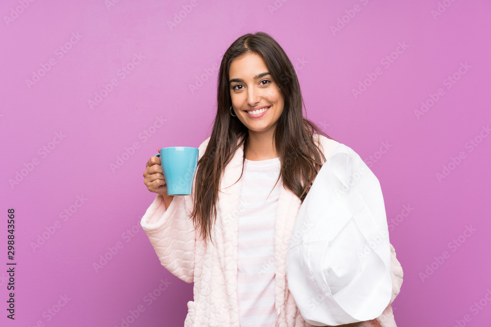 Young woman in pajamas and dressing gown over isolated purple background holding a cup of coffee Young woman in pajamas and dressing gown over isolated purple background holding a cup of coffee