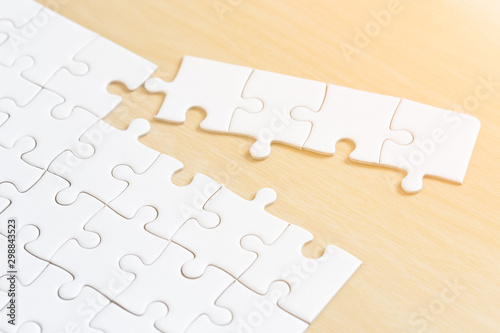 white connected jigsaw puzzle pieces on wooden table background.