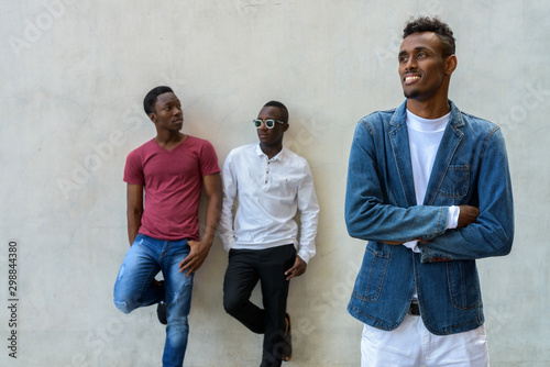 Three young African men hanging out against concrete wall outdoors