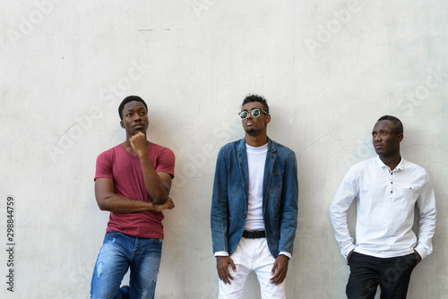 Three young African men hanging out against concrete wall outdoors