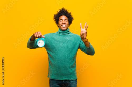 young african american man with an alarm clock against orange ba photo