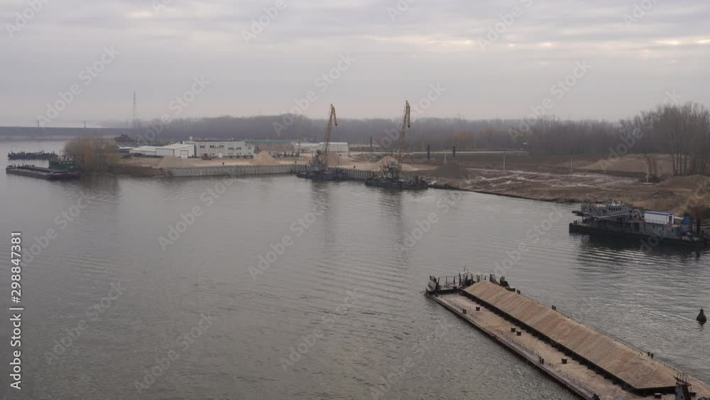 Barge with the inscription on Board (River), delivers crushed stone to the river cargo port under the unloading crane Barge with the inscription on Board (River), delivers crushed stone to the river cargo port under the unloading crane