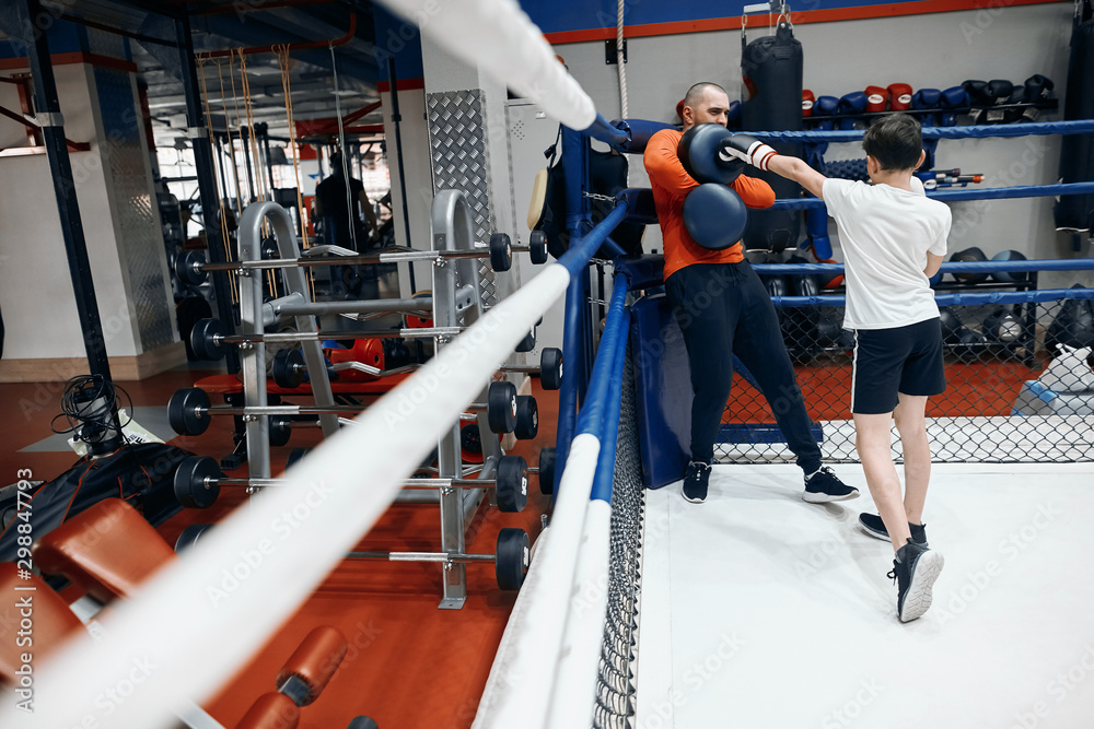 Little boy training with coach at sport club, when you are better than your coach. full length photo, young scared man standing in the corner of ring , he is being afrsid of strong kid
