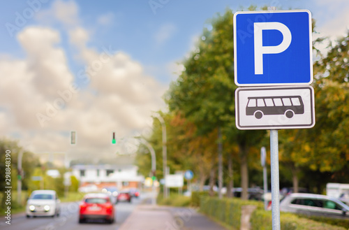 A rectangular blue and white sign with the letter P for parking. This parking is for buses only. A city street in the evening with cars and cloudy sky.