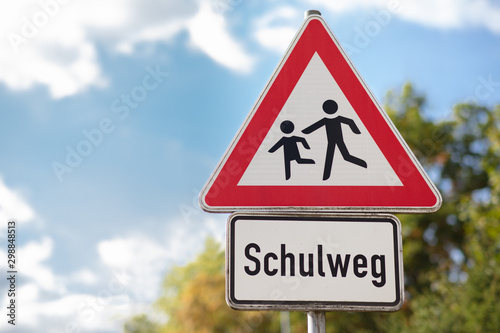 A triangular red and white warning sign depicting running children. It is a way to school. Translation on the sign: way to school.