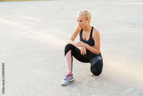 Image of sportswoman wearing tracksuit and earpods doing workout outdoors