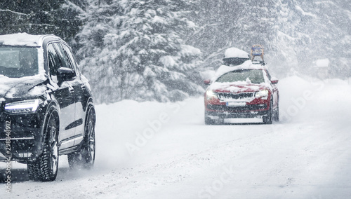 Winter road in beatiful forest. Snow calamity or blizzard. Fast cars on snowy roads in storm.