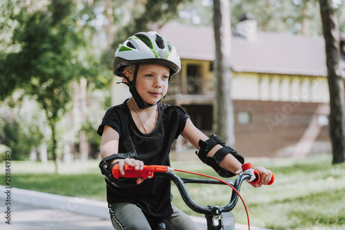 Cute little girl in safety helmet riding bicycle outdoors