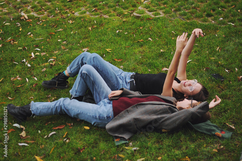 Two girls in blue jeans are lying on the grass