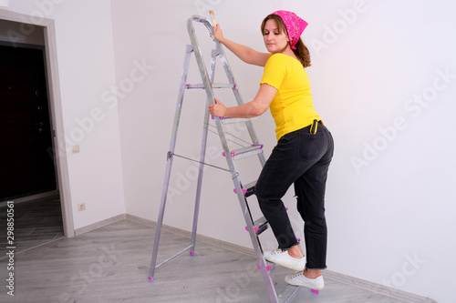 Woman house painter takes a step on ladder on white wall background.