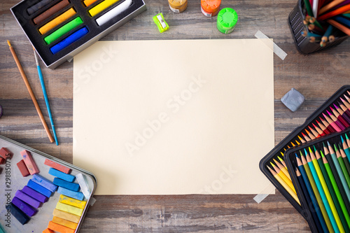 Flat lay top view of art workplace, wooden table with colored pencils, paper and crayon pastel chalks