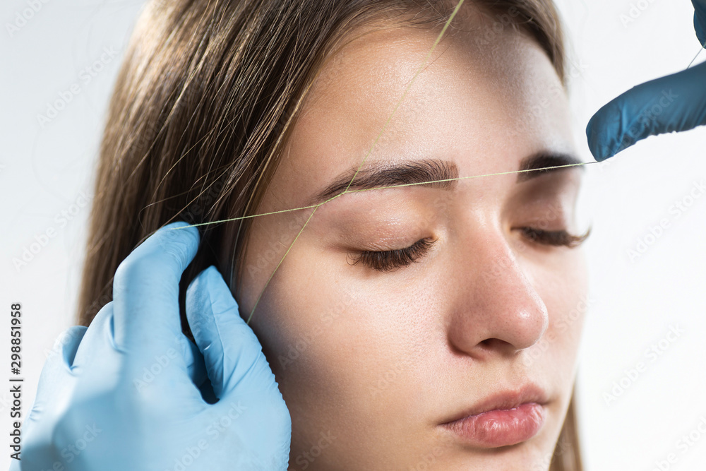 Cosmetologist plucks client eyebrows by thread