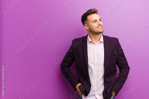 young hispanic man looking happy, cheerful and confident, smiling proudly and looking to side with both hands on hips