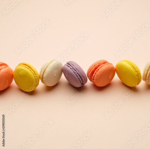 round multi-colored baked macarons with cream lie in a line on a beige background