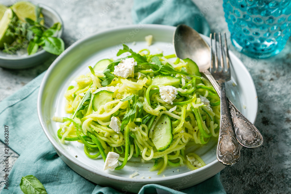 Zucchini noodles with cucumber, feta cheese and arugula, rustic background