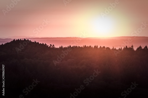 Wonderful magic sunshine over a german forest. Sunrise or sundown at the horizon of a large forest in Germany in europe. A very idyllic and magical scene with beautiful colors