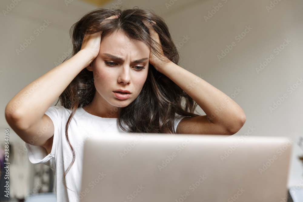 Image of puzzled woman grabbing her head and using laptop while sitting Image of puzzled woman grabbing her head and using laptop while sitting