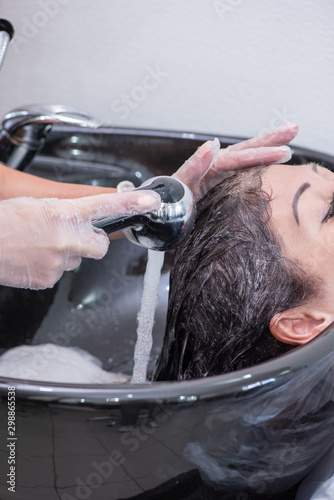 Head wash by a beautiful brunette woman in a black sink in a beauty salon