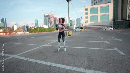 Wallpaper Mural Thin muscular woman exercising with dumbbell weights as part of her fitness workout. Slow motion shot in a parking lot with an urban skyline background. Torontodigital.ca