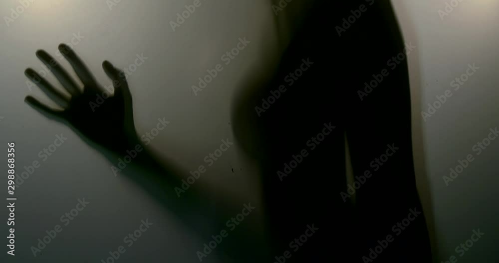 Close-up of the shadow of the body of a woman who touches the glass with her hands. The reflection of the silhouette through the light.