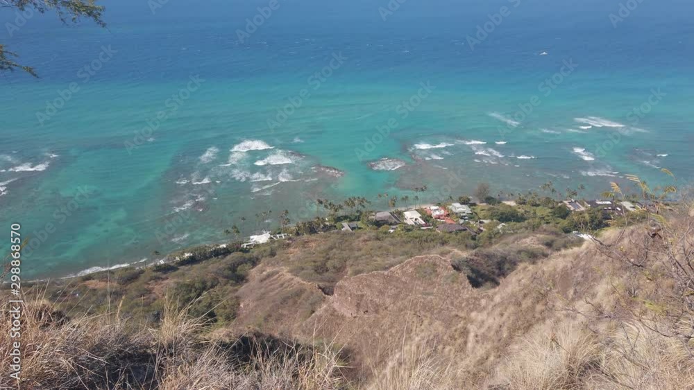 View from a mountain looking down at the sea and beach far below. Beautiful landscape of Hawaii with turquoise water and dramatic steep terrain rising up from the ocean.