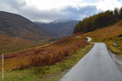 Single track road through Glen Etive, Scottish Highlands with snow capped mountains in background