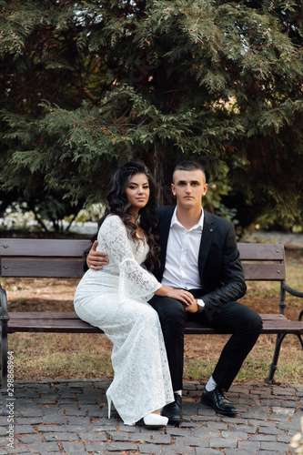 A man and a girl sitting on bench in the park. Cute couple embracing. A love story. Romantic moment. Girl in white dress and guy in suit. Beautiful couple in love. A love story.