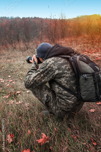 the photographer takes a photo in camouflage clothes on a background of autumn forest and sunset in the fog