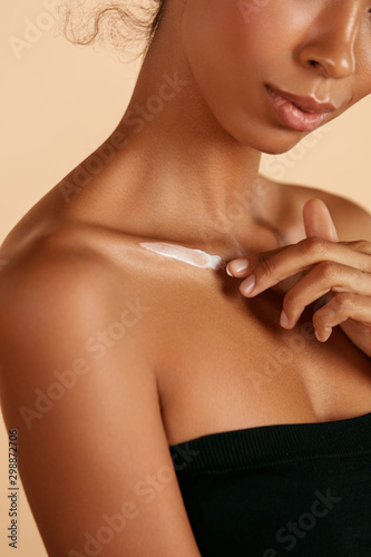 Skin care. Closeup woman s body with cosmetic cream on skin. Beautiful black girl with moisturizing lotion on hydrated body skin at studio