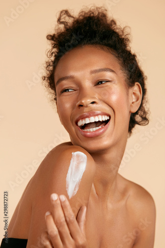 Body skin care. Smiling black woman applying body cream portrait. Beautiful h...