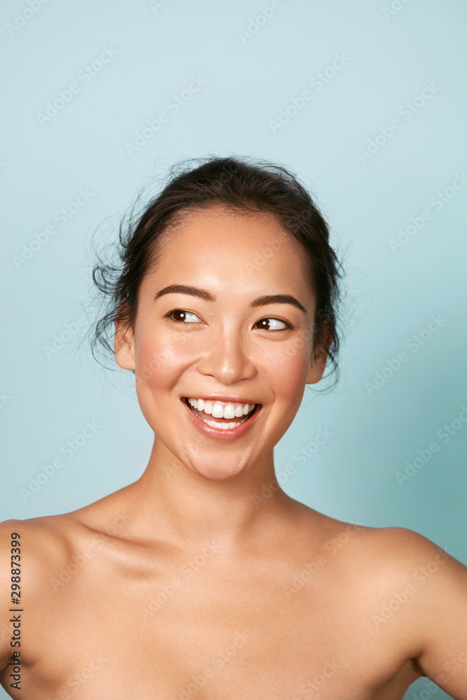 Foto de Beauty face. Smiling asian woman with perfect skin portrait.  Beautiful happy girl model with healthy glowing facial skin and natural  makeup and white smile on blue background at studio do