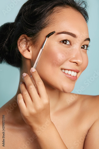 Makeup. Woman brushing brows with eyebrow brush closeup. Portrait of happy sm...