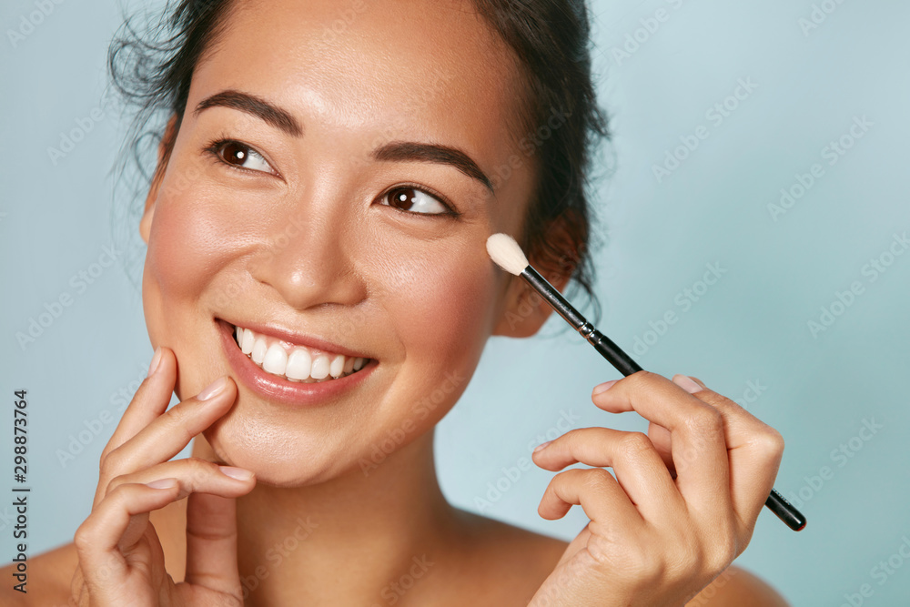 Beauty. Woman applying makeup on eyes with cosmetic brush closeup. Portrait  of happy smiling asian girl model with beautiful face applying facial make  up at studio Stock Photo | Adobe Stock