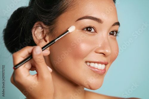 Beauty. Woman applying makeup on eyes with cosmetic brush closeup. Portrait o...