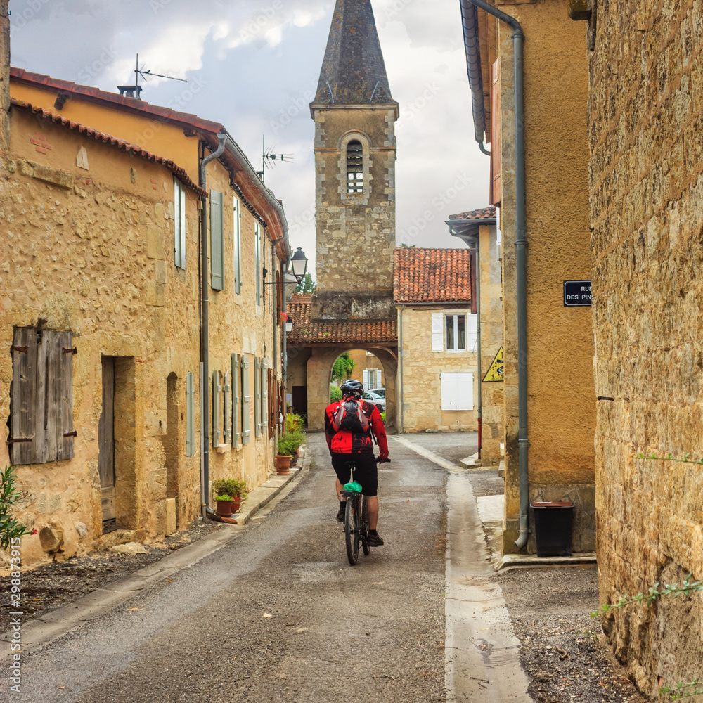 Summer city landscape - back view of a cyclist who rides down a medieval street, in the historical province Gascony, the region of Occitanie of southwestern France