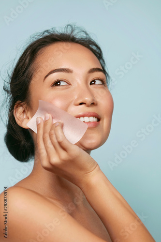 Face skin care. Smiling woman using facial oil blotting paper portrait. Close...