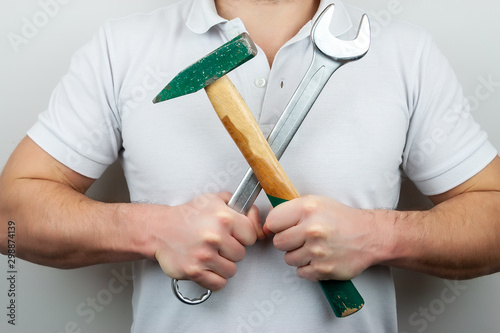 A man in a white t-shirt with a hammer and a wrench, holding them crosswise
